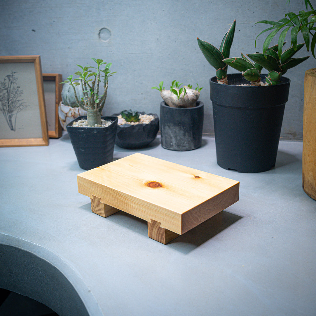 An overhead view of a wooden sushi tray placed on a gray kitchen counter. In the background, four small plants are visible, adding a touch of greenery to the scene.