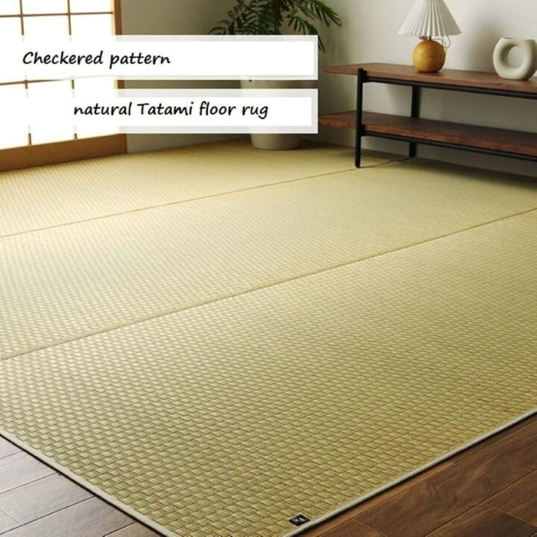 A natural tatami mat flooring is placed in the center of a western-style living room. A Japanese-style window is visible on the left, while a wooden bench with a lamp is placed on the right. The wall behind is painted white, creating a bright and serene atmosphere.