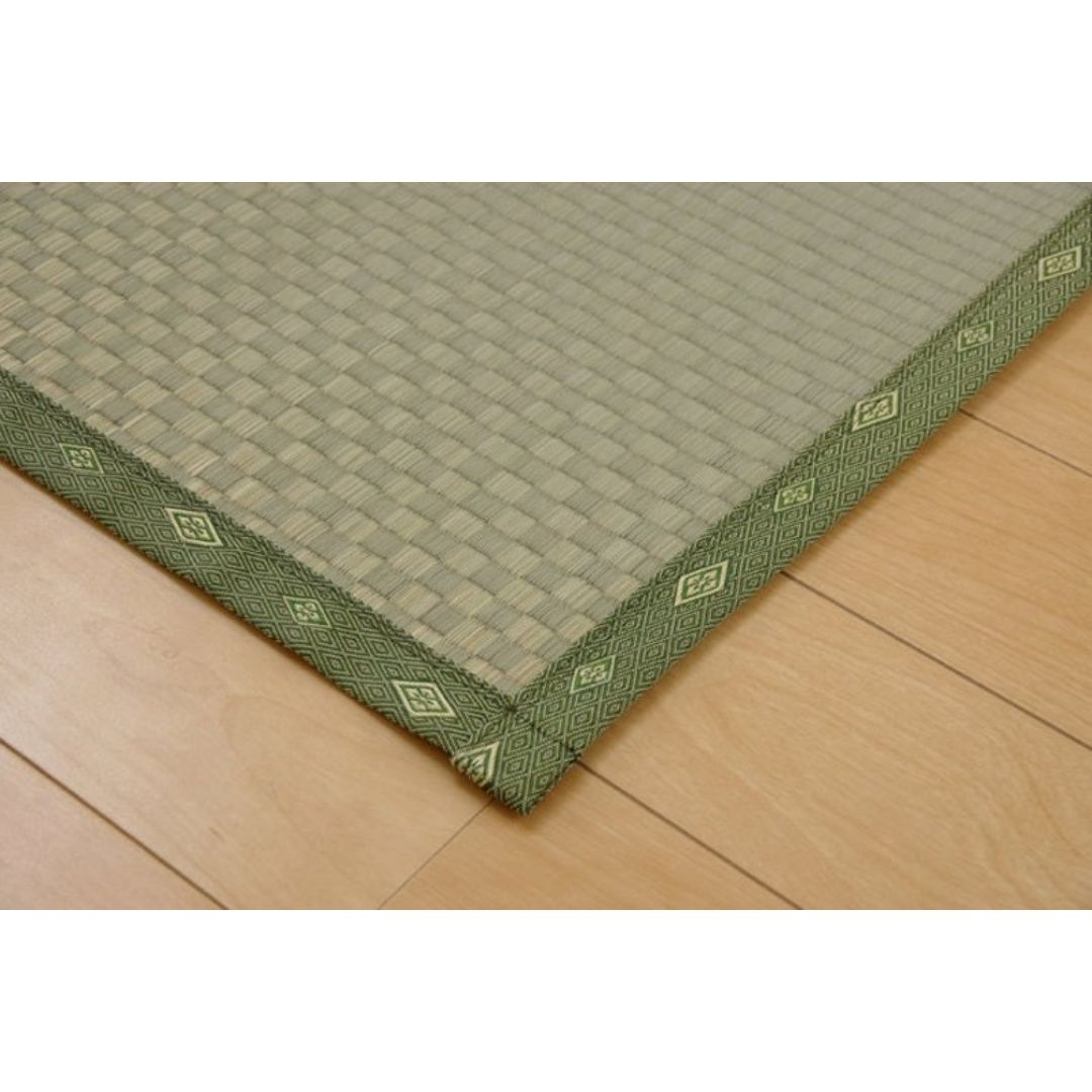 A corner of a green tatami mat made of natural rush grass laid on a wooden floor, with a subtle pattern of shadows created by the light shining through the window.