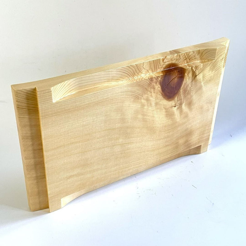 A wooden sushi tray is laid on its side on a white surface, with the back part prominently displayed in a vertical position. The tray features a red knot on its surface, adding a pop of color to the natural wood grain.