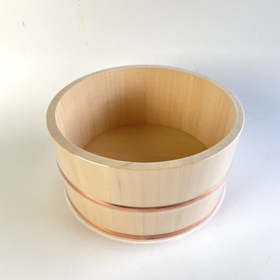 A wooden bath bucket with two copper rings around, placed in the center of a white room.