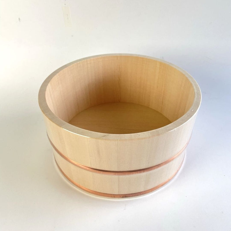 A wooden bath bucket with two copper rings around, placed in the center of a white room.